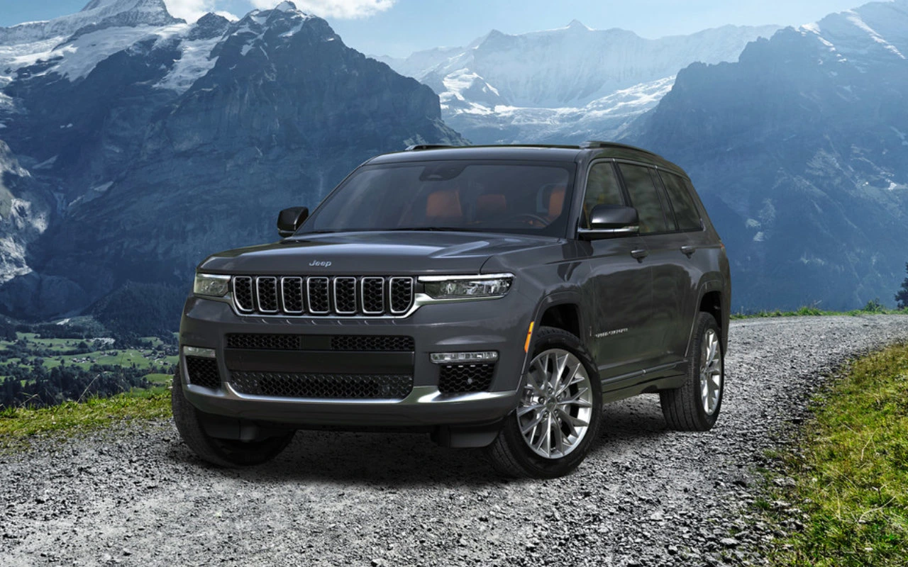 vue latérale avant d'un Jeep GRand Cherokee 2023 sur une route devant une chaine de montagnes