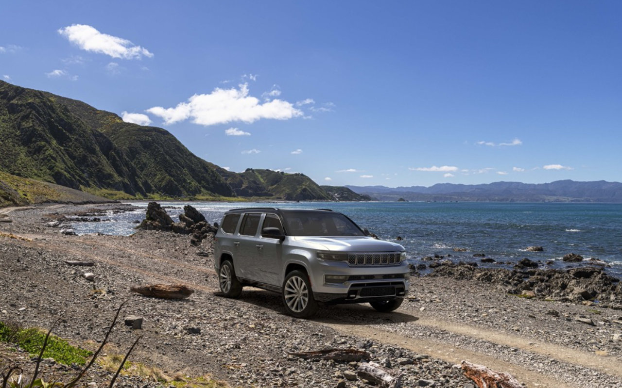 vue latérale avant d'un Grand Wagoneer 2023 sur un sentir au bord d'un grand lac