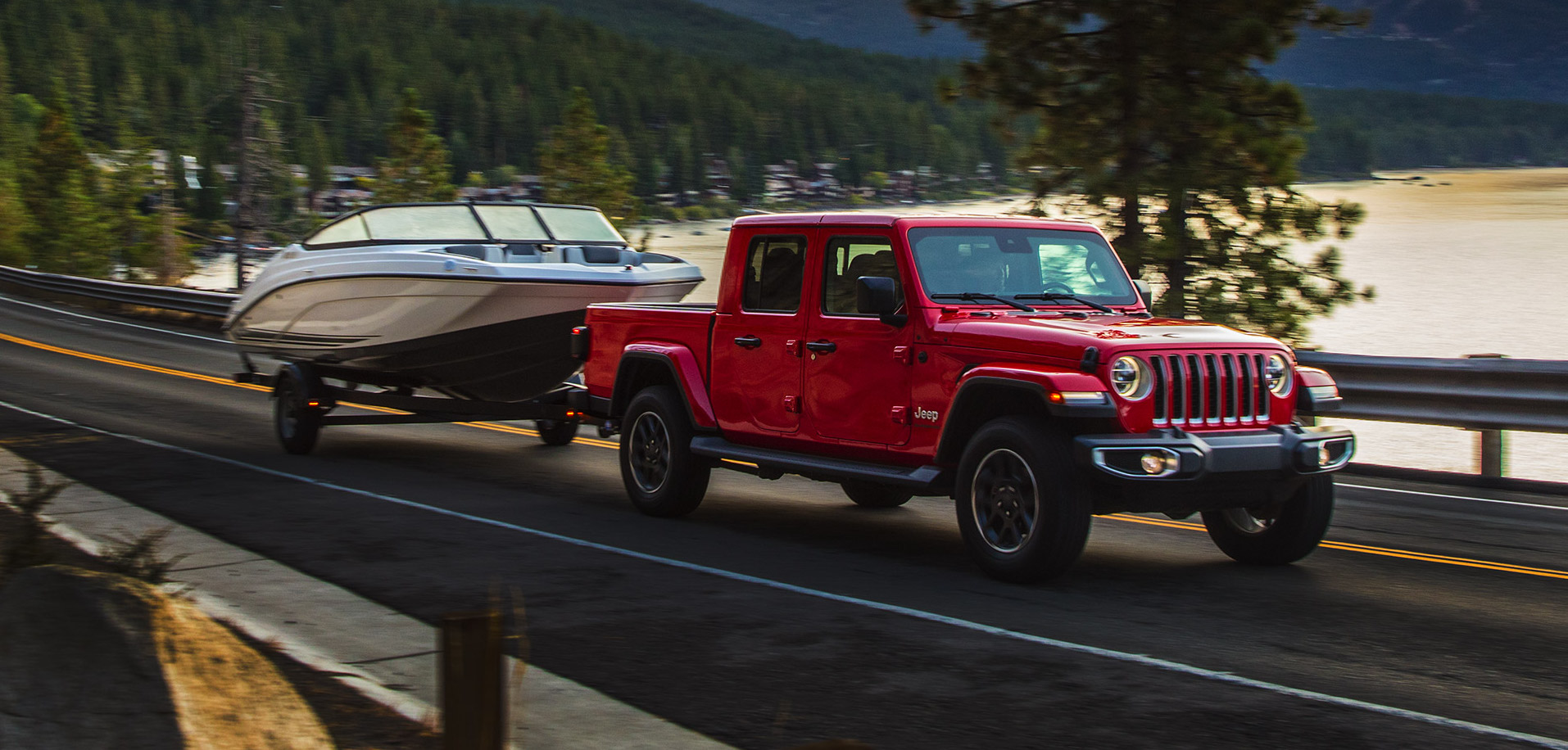 Jeep Gladiator Overland 2021 rouge remorquant un bateau sur l'autoroute au bord d'un lac