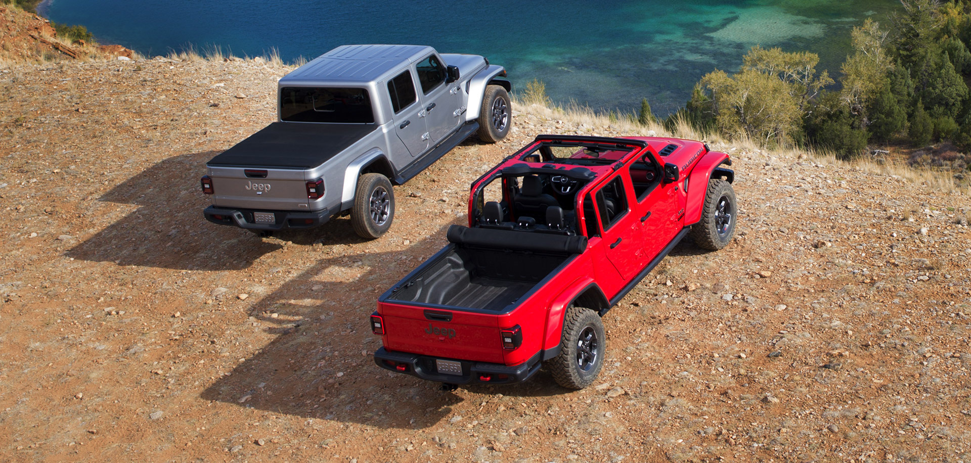 Jeep Gladiator Overland 2021 gris métallisé à gauche et le Jeep Gladiator Rubicon 2021 à droite, les 2 véhicules garés sur une terre de sable au bord d'un lac